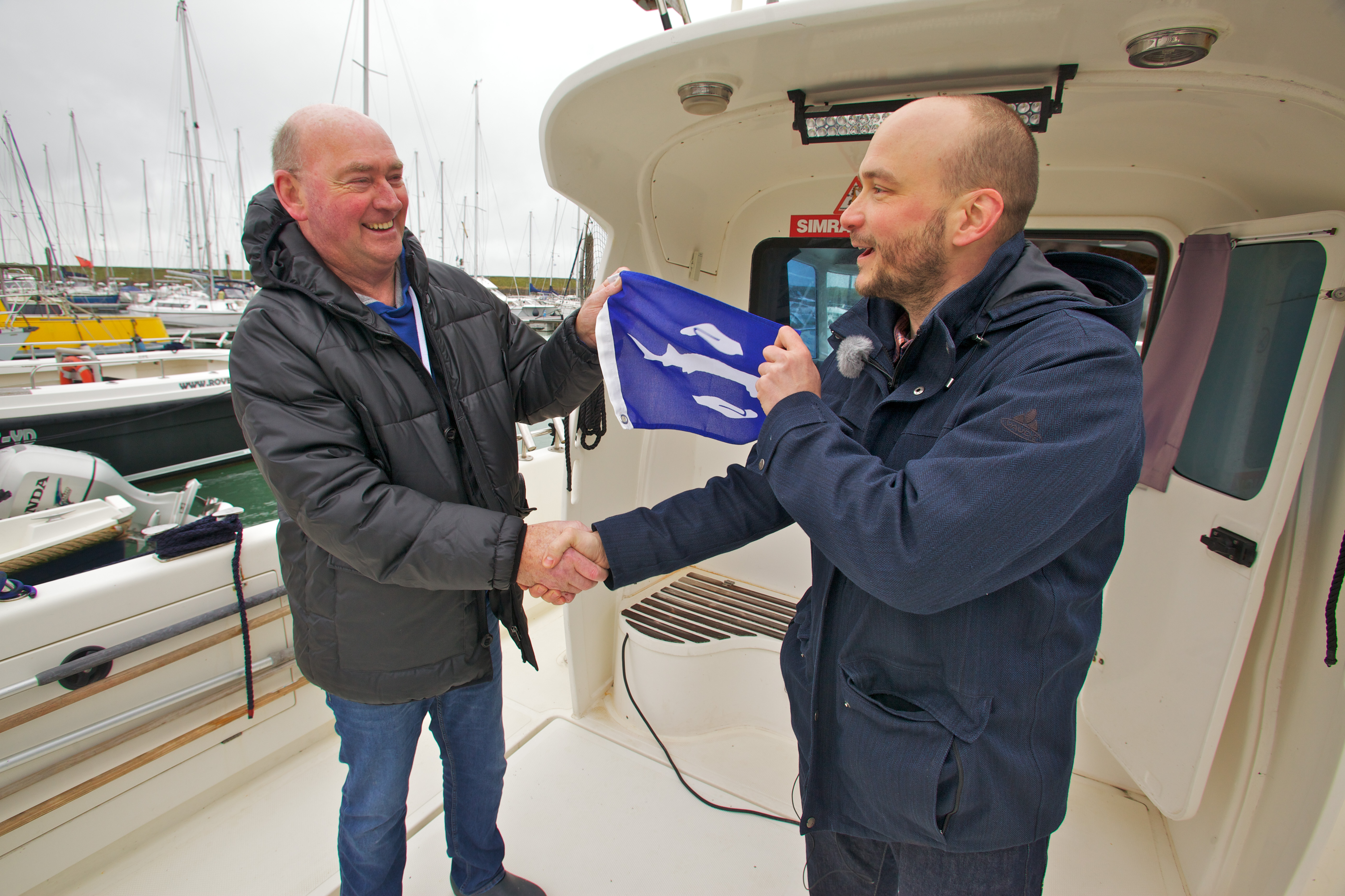 Schipper Sjef Mathijssen (links) ontvangt de eerste steurenvlag van Bram Houben van ARK Natuurontwikkeling