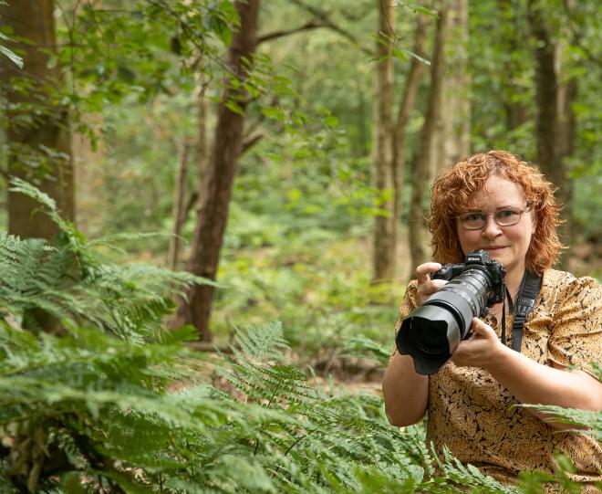 Mignon van den Wittenboer terwijl ze met haar fotocamera opnamen aan het maken is in een varenrijk loofbos.