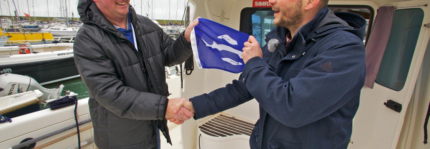 Schipper Sjef Mathijssen (links) ontvangt de eerste steurenvlag van Bram Houben van ARK Natuurontwikkeling
